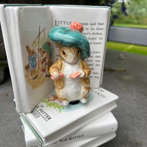Peut inclure: Un serre-livres en céramique avec une figurine de Pierre Lapin portant un chapeau vert. Le serre-livres est composé de livres blancs empilés avec du texte de l'histoire. Édition sous licence.
