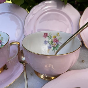 May include: A set of pink teacups and saucers with floral designs and gold trim. The set includes a teapot, sugar bowl, creamer, and four teacups and saucers.