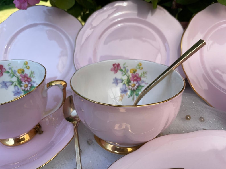 May include: A set of pink teacups and saucers with floral designs and gold trim. The set includes a teapot, sugar bowl, creamer, and four teacups and saucers.