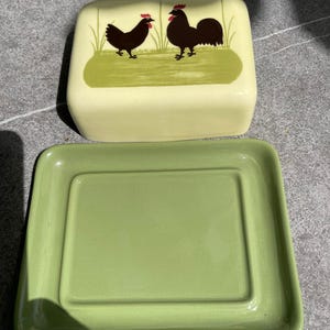 Peut inclure: Un beurrier en c&eacute;ramique vert avec un couvercle. Le couvercle repr&eacute;sente un coq et une poule noirs avec des cr&ecirc;tes rouges, debout sur un champ vert.