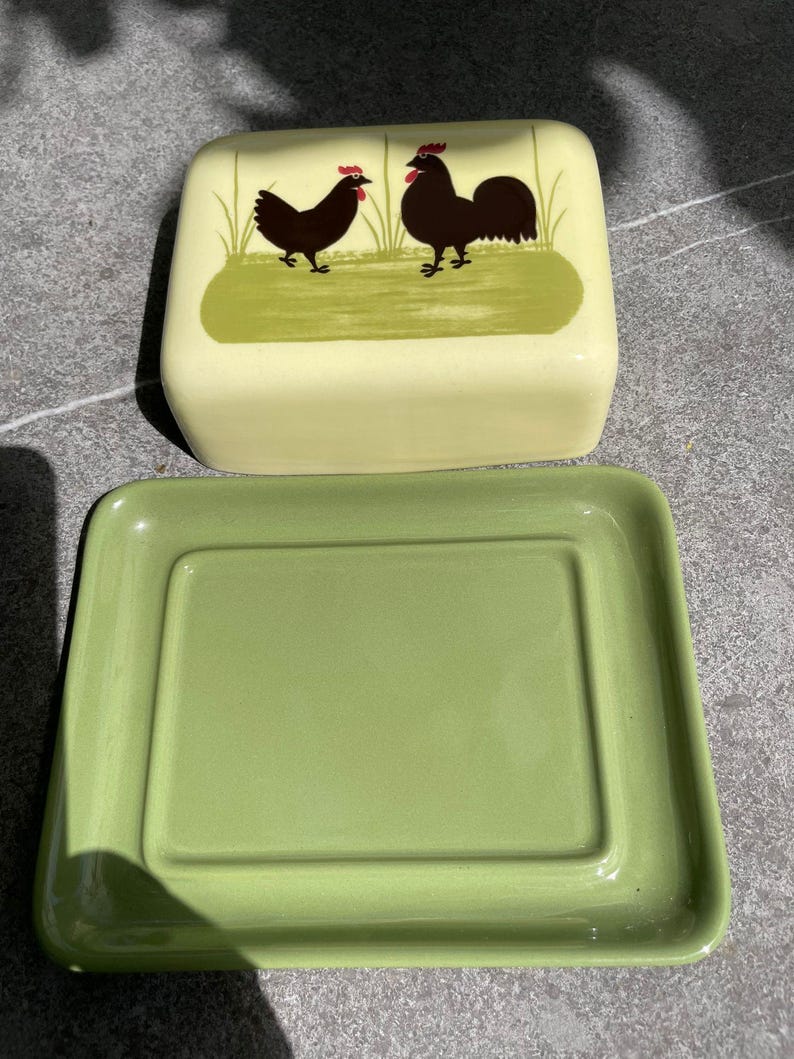 Peut inclure: Un beurrier en c&eacute;ramique vert avec un couvercle. Le couvercle repr&eacute;sente un coq et une poule noirs avec des cr&ecirc;tes rouges, debout sur un champ vert.