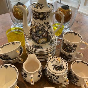 Könnte beinhalten: Ein Vintage-Teeservice mit einem schwarz-weißen Blumendesign. Das Set umfasst eine Teekanne, Tassen, Untertassen, einen Sahnekännchen und eine Zuckerdose. Die Teekanne hat einen langen, gebogenen Ausguss und einen dekorativen Deckel.