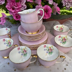 May include: A pink and white tea set with floral designs. The set includes a teapot, creamer, sugar bowl, and six teacups and saucers.