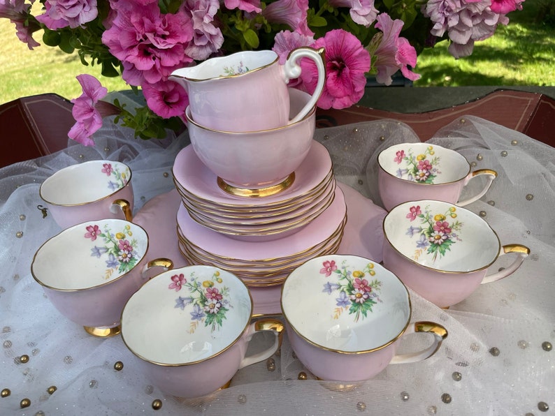 May include: A pink and white tea set with floral designs. The set includes a teapot, creamer, sugar bowl, and six teacups and saucers.