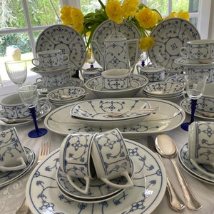 Könnte beinhalten: Ein weiß-blaues Porzellan-Geschirr-Set mit einem zarten Blumenmuster. Das Set enthält Teller, Schalen, Tassen, Untertassen, eine Teekanne, eine Zuckerdose und eine Milchkännchen.