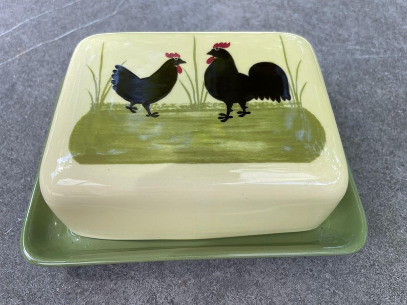 Peut inclure: Un beurrier en c&eacute;ramique vert avec un couvercle repr&eacute;sentant un coq et une poule noirs peints sur un fond vert.