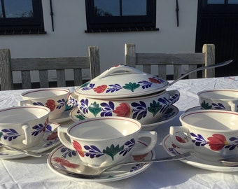 Peut inclure: Un ensemble de six bols à soupe blancs avec des motifs floraux bleus, verts et rouges. Les bols sont disposés sur une nappe blanche avec une cuillère de service en argent et une soupière assortie.