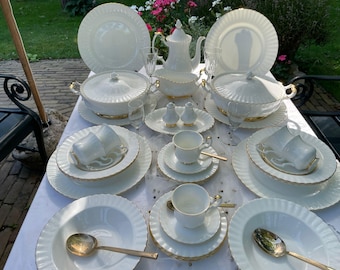May include: A white porcelain dinnerware set with gold trim. The set includes a variety of plates, bowls, and serving dishes.