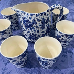 May include: A set of blue and white ceramic cups and a pitcher with a floral pattern. The cups and pitcher have a white interior and a blue and white floral design on the exterior.