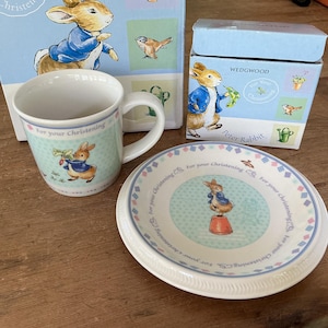 Puede incluir: Un juego de regalo para bebés con el tema de Peter Rabbit. El juego incluye una taza, un plato y dos cajas. La taza y el plato tienen un fondo azul claro con ilustraciones de Peter Rabbit.