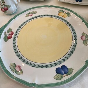 May include: A large round ceramic serving platter with a scalloped edge and a green rim. The centre is pale yellow, surrounded by a green leaf border. The white border features illustrations of cherries, lemons, plums, and flowers.