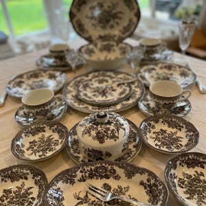 May include: A set of brown and white floral patterned china dinnerware, including plates, bowls, cups, and saucers. The set features a delicate floral design with a brown and white colour scheme.
