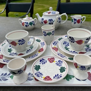 Può includere: Un set da tè bianco con motivi floreali blu e rossi. Il set comprende una teiera, un creamer, uno zuccheriera, due tazze, due piattini e due porta uova.