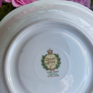 May include: White saucer with a green and gold Queen Anne Fine Bone China England logo in the center.