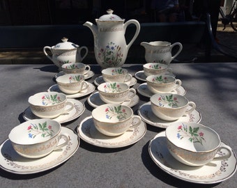May include: A vintage white tea set with floral designs and gold accents. The set includes a teapot, creamer, sugar bowl, and 10 teacups and saucers.