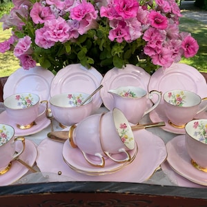 May include: A pink tea set with floral designs on the cups and saucers. The set includes a teapot, creamer, sugar bowl, and six teacups and saucers.