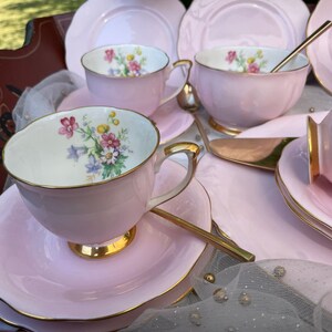 May include: A pink tea set with floral designs on the cups and saucers. The set includes a teapot, creamer, sugar bowl, and four teacups and saucers.