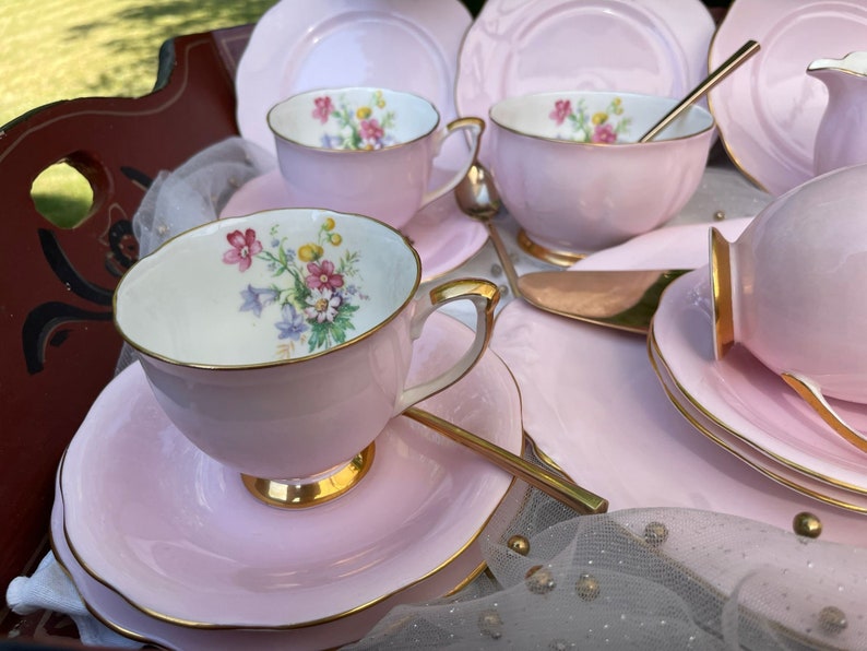 May include: A pink tea set with floral designs on the cups and saucers. The set includes a teapot, creamer, sugar bowl, and four teacups and saucers.