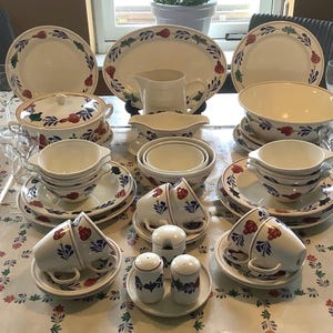 Könnte beinhalten: Ein Set weißer Keramikgeschirr mit blauen und roten Blumendesigns. Das Set beinhaltet eine große Schüssel, eine Servierplatte, eine Sauciere, ein Set Teetassen und Untertassen sowie ein Set Salz- und Pfefferstreuer.