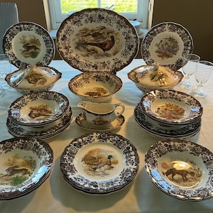 Könnte beinhalten: Ein komplettes Vintage-Geschirrset mit braunen und weißen Blumen- und Wildtiermotiven. Das Set umfasst Teller, Schalen, Servierschalen und eine Sauciere. Die Teller und Schalen haben einen dekorativen braunen Rand.