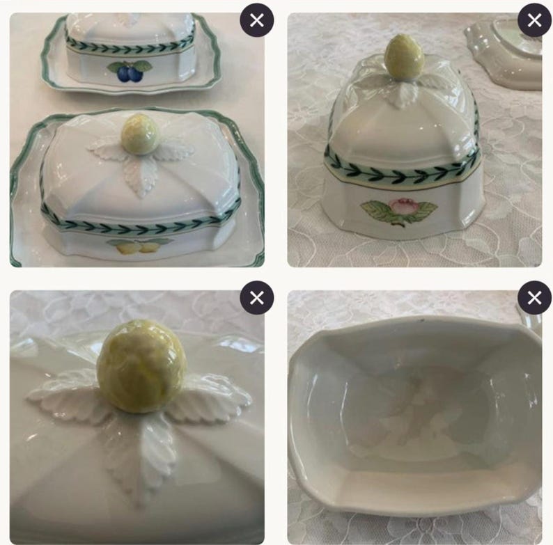 May include: A white ceramic butter dish with a lid featuring a yellow fruit-shaped handle, green leaf accents, and a green border. The dish is decorated with various fruit illustrations including plums, lemons, and a pink flower on the sides.