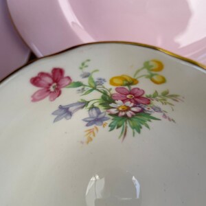 May include: A white teacup with a floral design featuring pink, yellow, and blue flowers. The teacup has a gold rim.