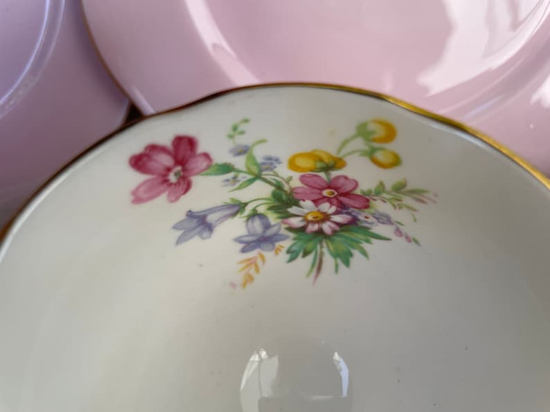 May include: A white teacup with a floral design featuring pink, yellow, and blue flowers. The teacup has a gold rim.