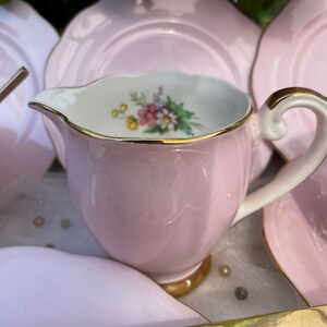 May include: A pink tea set with a floral design and gold trim. The set includes a teapot, creamer, sugar bowl, and four cups and saucers.