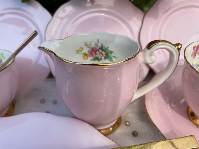 May include: A pink tea set with a floral design and gold trim. The set includes a teapot, creamer, sugar bowl, and four cups and saucers.