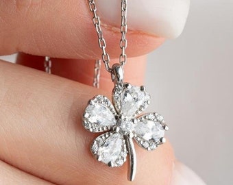Puede incluir: Un collar de plata con un colgante de trébol de cuatro hojas engastado con piedras de circonita cúbica transparentes.