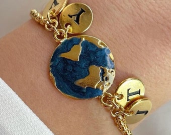 May include: Gold charm bracelet with a blue and gold globe charm and letter charms. The bracelet is on a person's wrist.