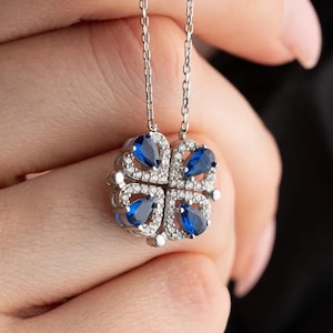 May include: A silver necklace with a blue and white clover pendant. The pendant is made of small, sparkling stones.