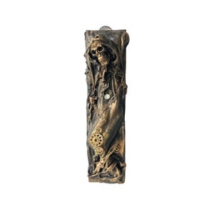 May include: A bronze-colored, rectangular sculpture featuring a hooded skull figure. The sculpture incorporates gears, chains, and a pocket watch, with a textured, aged appearance. The overall theme is gothic and steampunk.