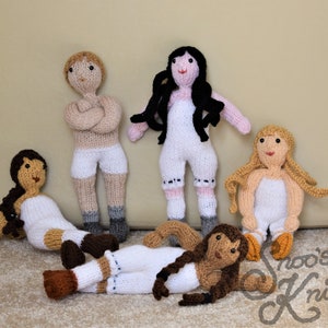May include: Five knitted dolls, each with a different hair color and outfit. The dolls are all wearing white dresses or pants and have painted faces. The dolls are sitting on a beige surface.