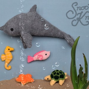 May include: A collection of handmade knitted sea creatures, including a gray dolphin, a yellow seahorse, a pink fish, an orange starfish, and a green turtle. The background is a light blue with bubbles and the text "Snoo's Knits".