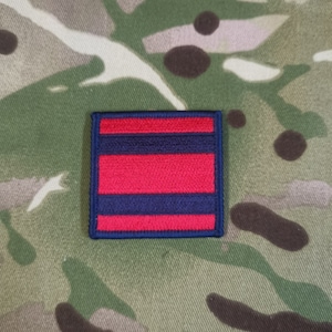 May include: A woven patch with three horizontal stripes in red and blue. The top and bottom stripes are blue, and the middle stripe is red.