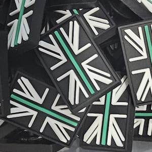 Könnte beinhalten: Ein Haufen schwarzer rechteckiger Aufnäher mit einem stilisierten Union Jack-Design. Das Design umfasst weiße und grüne Akzente auf schwarzem Hintergrund. Die Aufnäher sind wahrscheinlich für Kleidung oder Accessoires.