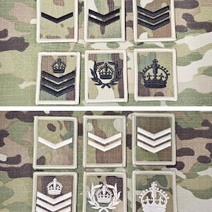 May include: A collection of military rank insignia patches. The patches feature camouflage backgrounds with chevrons and crown emblems in various designs. The patches are rectangular with white borders.