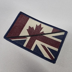 May include: A rectangular patch combining the Canadian flag and the Union Jack. The design features a navy blue border, with the Canadian maple leaf and the Union Jack's elements in burgundy, off-white, and navy blue.