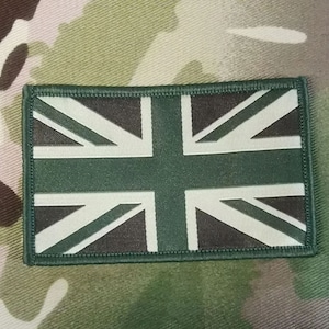 Peut inclure: Un patch de drapeau Union Jack vert et blanc avec une bordure cousue. Le patch est en tissu et a un fond de camouflage.