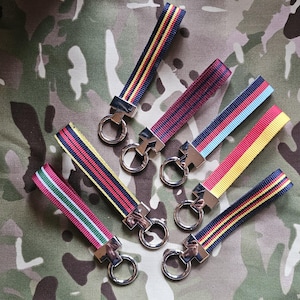 May include: Seven keychains with different coloured ribbon straps and silver key rings. The ribbons are red, yellow, blue, green, black, and white.