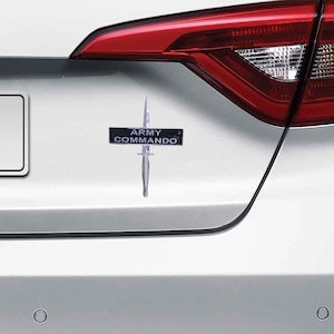 May include: A white car with a black and silver sticker that says "Army Commando" with a silver knife image.