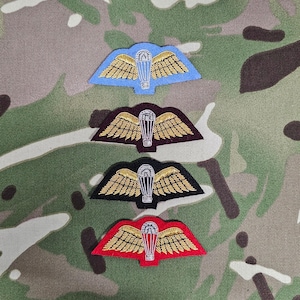 May include: Four embroidered patches with gold wings and a silver parachute in the center. The patches are on a camouflage background. The patches are in the colors blue, maroon, black, and red.