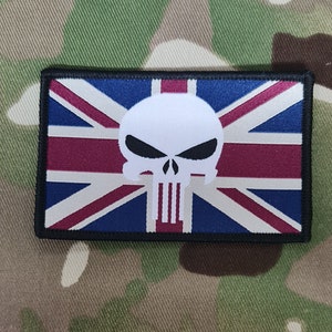 Op de afbeelding: Een zwart-witte schedel met een rood, wit en blauwe Union Jack-vlag op de achtergrond. De schedel is gecentreerd op de vlag. De vlag is een patch met een zwarte rand.