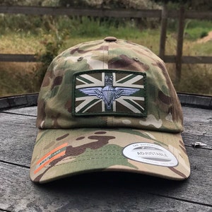 May include: A camouflage baseball cap with a green, white and red patch featuring a parachute and the Union Jack. The cap is adjustable and has a "The Authentic" label.