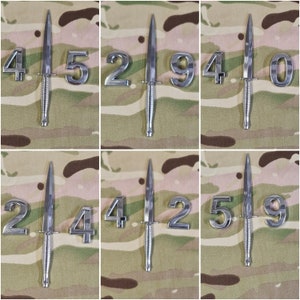 May include: Nine silver-colored metal numbers, 4, 5, 2, 9, 4, 0, 2, 4, 2, 5, 9, are arranged in a grid pattern. Each number is attached to a small silver-colored knife with a black handle.