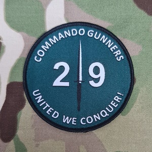 Könnte beinhalten: Ein runder, grüner Aufnäher mit schwarzen Nähten. Es steht "Commando Gunners 219 United We Conquer!" in weißer Schrift um den Rand. Ein schwarzer Dolch befindet sich in der Mitte.