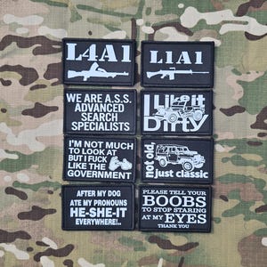 May include: A collection of eight rectangular black morale patches with white text and graphics. The patches feature various slogans and illustrations, including rifles, a jeep, and humorous phrases such as 'I Like it Dirty' and 'Not Old, Just Classic'.
