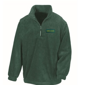 Könnte beinhalten: Ein dunkelgrüner Fleece-Pullover mit Reißverschluss und einem Aufnäher auf der Brust, auf dem "AMBULANCE" in gelben Buchstaben steht.