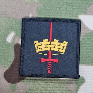 Könnte beinhalten: Ein schwarzer gestickter Aufnäher mit einer goldenen Krone und einem roten Schwert. Die Krone hat ein Ziegelmuster.